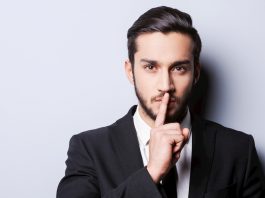 Mann hält Finger als Sperrvermerk vor seine Lippen.