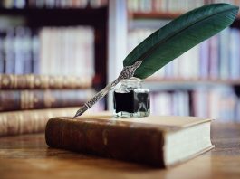 Eine edle Schreibfeder und ein Tintenfass platziert auf einem alten Buch