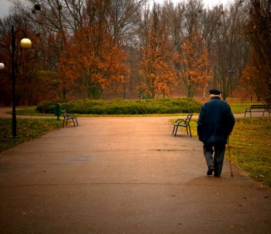 Armer alter Mann mit Krückstock geht durch den Park