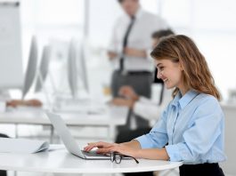 Eine Frau sitzt nur mit Laptop an einem Tisch in einem Büro mit Clean-Desk-Policy