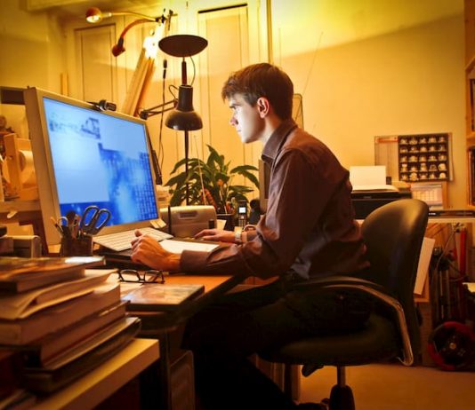 Ein Mann sitzt im Home-Office am PC und arbeitet aufgrund der Vertrauensarbeitszeit in der Nacht