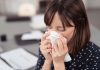 Eine kranke Frau niest auf der Arbeit in ein Taschentusch