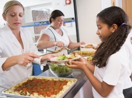 Eine Frau hat einen 1-Euro-Job und teilt Essen an Schulkinder in der Mensa aus