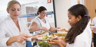 Eine Frau hat einen 1-Euro-Job und teilt Essen an Schulkinder in der Mensa aus