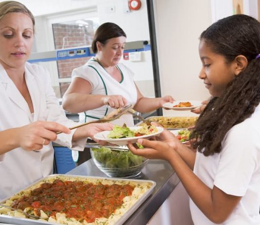 Eine Frau hat einen 1-Euro-Job und teilt Essen an Schulkinder in der Mensa aus