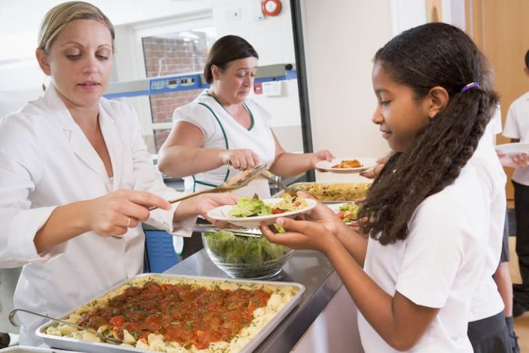 Eine Frau hat einen 1-Euro-Job und teilt Essen an Schulkinder in der Mensa aus