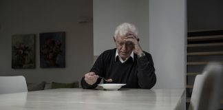 Ein Mann leidet am Empty-Desk-Syndrom und sitzt alleine Zuhause am Tisch und ist traurig