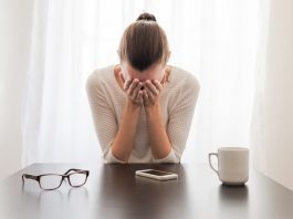 Eine Frau sitzt am Tisch und ist traurig, denn sie leidet unter der Doppelbelastung durch Familie und Beruf