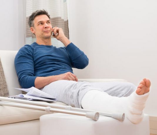 Ein Mann mit gebrochenem Bein telefoniert, er erhält Krankengeld