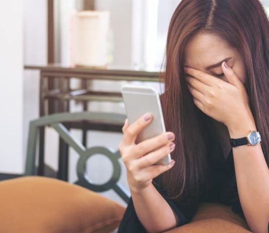 Eine Frau hält ein Smartphone und ist traurig durch Cybermobbing