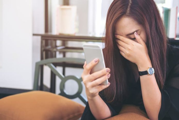 Eine Frau hält ein Smartphone und ist traurig durch Cybermobbing