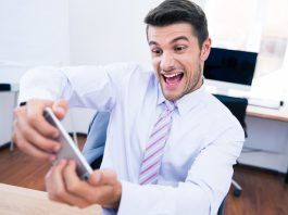 Ein Mann spielt mit seinem Smartphone auf der Arbeit, das kann eine Pflichtverletzung im Job sein