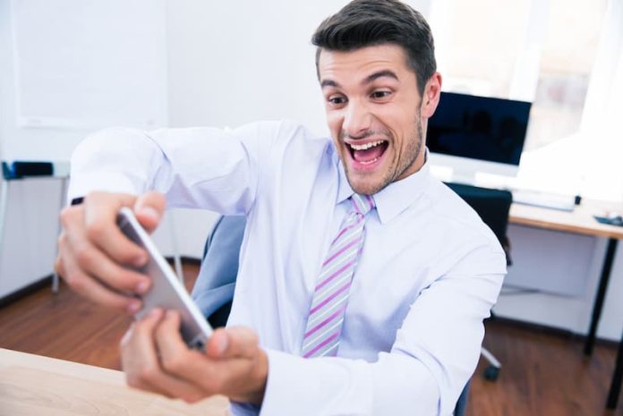 Ein Mann spielt mit seinem Smartphone auf der Arbeit, das kann eine Pflichtverletzung im Job sein