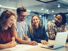 Mehrere glückliche Mitarbeiter an einem Tisch, welchen Zweck hat Employer Branding?