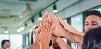 Mehrere Menschen halten die Hände zusammen, wie lässt sich Teamgeist fördern?