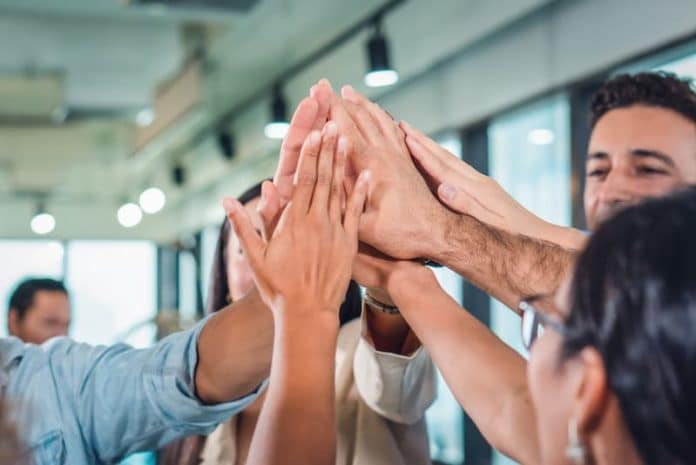 Mehrere Menschen halten die Hände zusammen, wie lässt sich Teamgeist fördern?
