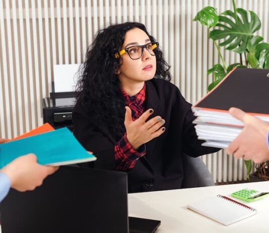 Eine Frau erhält viele Ordner gereicht, was lässt sich tun gegen ungerechte Behandlung am Arbeitsplatz?