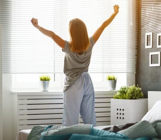 Eine Frau streckt sich am Fenster, wie kann man früh Aufstehen lernen?