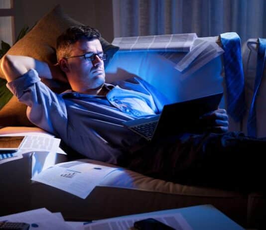 Ein Mann liegt mit Arbeitsunterlagen auf dem Sofa, er ist ein Workaholic