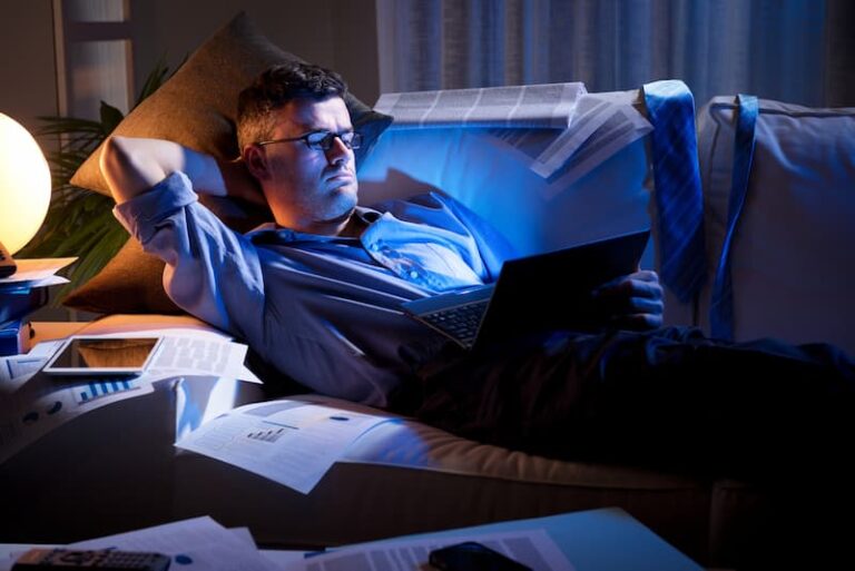 Ein Mann liegt mit Arbeitsunterlagen auf dem Sofa, er ist ein Workaholic