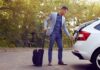 Ein Mann mit einem Koffer öffnet das Auto, was bedeutet Reisebereitschaft in der Bewerbung?