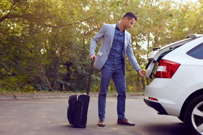 Ein Mann mit einem Koffer öffnet das Auto, was bedeutet Reisebereitschaft in der Bewerbung?