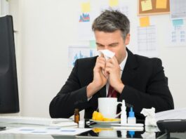 Ein Mann putzt sich die Nase am Arbeitsplatz, was ist Präsentismus?