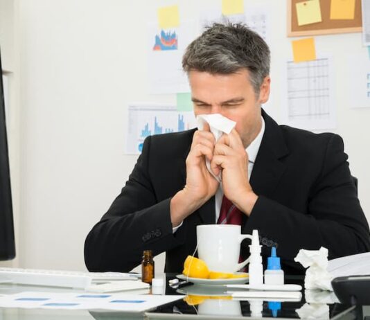 Ein Mann putzt sich die Nase am Arbeitsplatz, was ist Präsentismus?