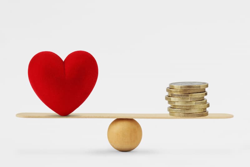 Ein Herz und Münzen auf einer WIppe, wie kann man sich zwischen Geld oder Freizeit entscheiden?