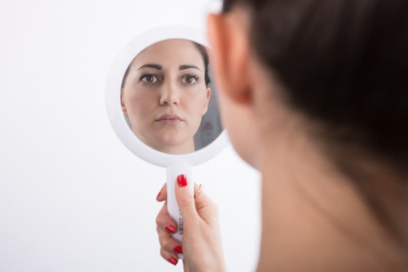 Eine Frau blickt in den Spiegel, wieso braucht man eine gute Selbsteinschätzung?