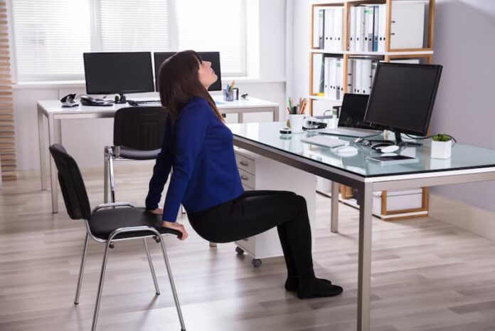 Eine Frau macht eine Übung mit einem Stuhl, welche Möglichkeiten gibt es bei der Bewegung am Arbeitsplatz?