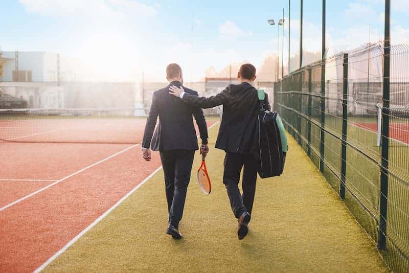 Zwei Männer im Anzug mit Tennisschlägern, was ist Sport nach der Arbeit?