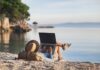 Eine Frau mit Laptop am Strand, was ist beim mobilen Arbeiten im Ausland zu beachten?