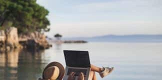 Eine Frau mit Laptop am Strand, was ist beim mobilen Arbeiten im Ausland zu beachten?