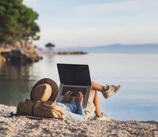Eine Frau mit Laptop am Strand, was ist beim mobilen Arbeiten im Ausland zu beachten?