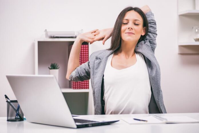 Eine Frau streckt sich im Büro, was ist Selbstfürsorge im Job?