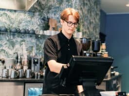 Ein Schüler steht im Bistro hinter der Kasse. Er übt einen Schülerjob aus.