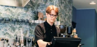 Ein Schüler steht im Bistro hinter der Kasse. Er übt einen Schülerjob aus.
