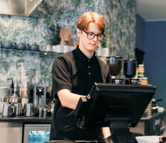 Ein Schüler steht im Bistro hinter der Kasse. Er übt einen Schülerjob aus.