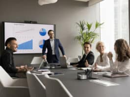 Ein Projektleiter hat ein Meeting mit Beschäftigten. Sie sind motiviert und freuen sich über den Unternehmenserfolg, da es Aktienoptionen für Mitarbeiter gibt.