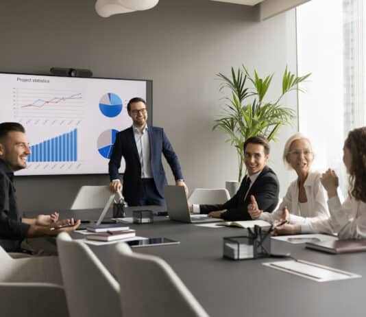 Ein Projektleiter hat ein Meeting mit Beschäftigten. Sie sind motiviert und freuen sich über den Unternehmenserfolg, da es Aktienoptionen für Mitarbeiter gibt.