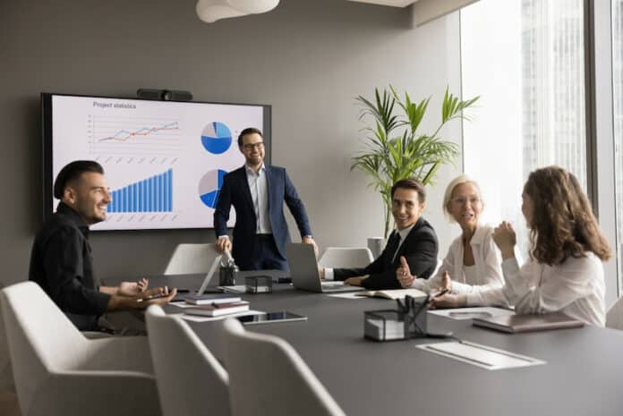 Ein Projektleiter hat ein Meeting mit Beschäftigten. Sie sind motiviert und freuen sich über den Unternehmenserfolg, da es Aktienoptionen für Mitarbeiter gibt.