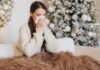 Eine Frau hat Schnupfen und sitzt mit einer Decke auf dem Sofa vor einem Weihnachtsbaum. Sie leidet in ihrem Weihnachtsurlaub unter Leisure Sickness.