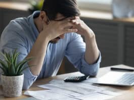 Mann sitzt mit den Händen im Gesicht am Schreibtisch. Er hat Angst vor der Arbeit.
