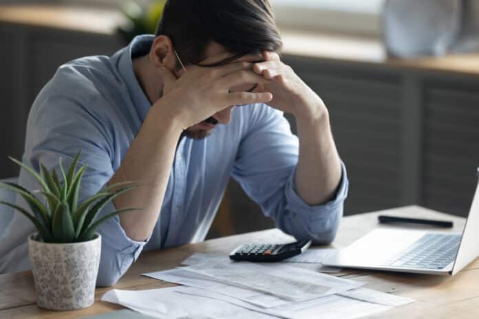 Mann sitzt mit den Händen im Gesicht am Schreibtisch. Er hat Angst vor der Arbeit.