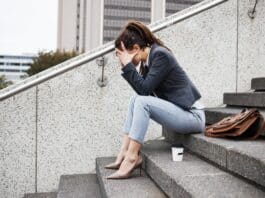 Frau sitzt auf einer Betontreppe. Das Gesicht in den Händen versteckt, weil sie Angst hat, keinen Job zu finden.