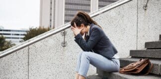 Frau sitzt auf einer Betontreppe. Das Gesicht in den Händen versteckt, weil sie Angst hat, keinen Job zu finden.