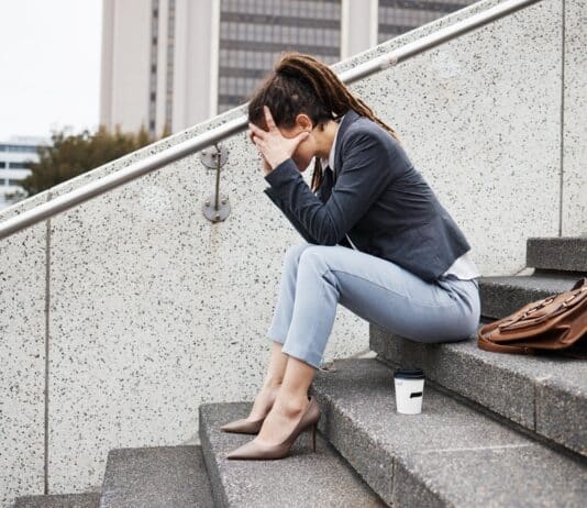 Frau sitzt auf einer Betontreppe. Das Gesicht in den Händen versteckt, weil sie Angst hat, keinen Job zu finden.