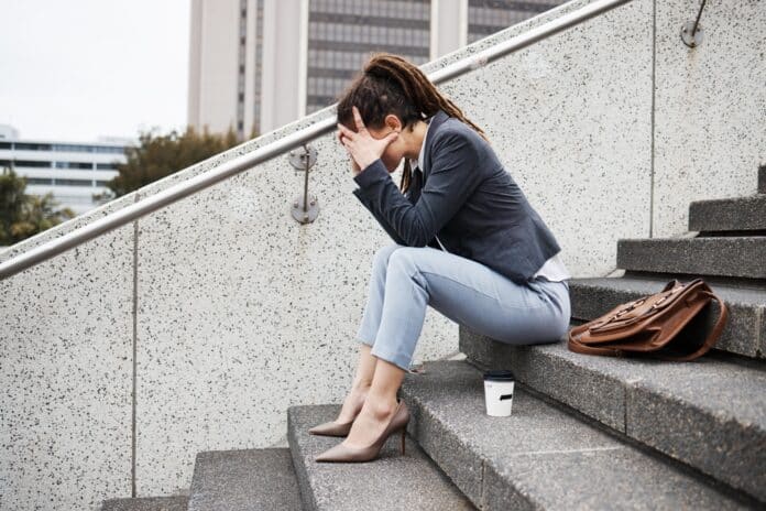 Frau sitzt auf einer Betontreppe. Das Gesicht in den Händen versteckt, weil sie Angst hat, keinen Job zu finden.