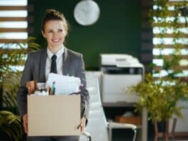 Eine Frau trägt einen Karton mit Büromaterial. Sie freut sich auf den Neuanfang nach ihrer Kündigung.